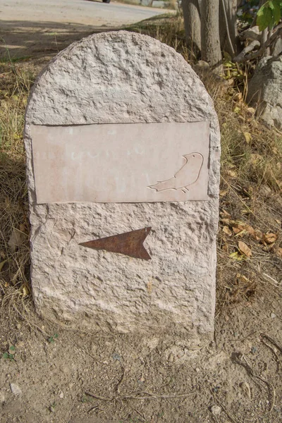 a stone marker next to a path with an arrow and a carved bird