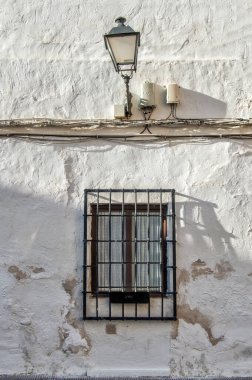 Eski sokak lambalı beyaz duvar, ışık kabloları ve metal ızgaralı pencere.