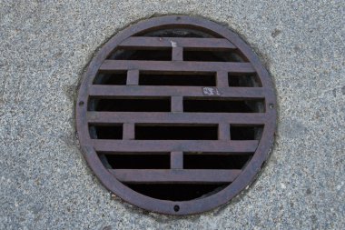 Sokakta granit bir zeminde izole edilmiş dairesel metal drenaj ızgarası.