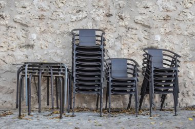 Bar masaları ve sandalyeler taş bir duvarın yanında ve yerde kurumuş yapraklar.