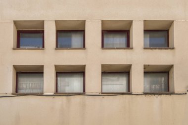 Açık kahverengi bir duvarda sekiz kare pencere deseni oluşuyor.