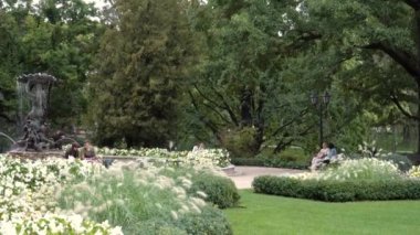 Riga, Letonya - 25 Ağustos 2023. İnsanlar yeşillik bir alanda dinleniyor. İnsanlar, Letonya 'nın tarihi başkentindeki heykel suyu pınarının yanındaki Opera Meydanı' nda dinleniyorlar..