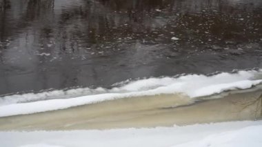 Bu, kışın donmuş nehir kıyısındaki su akışının yakın görüntüsü. Nehir kıyısındaki buzlu donmuş sanat akıntısının akıntısıyla çelişiyor.. 