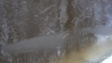 Yağan kar manzaralı kışın sağanak yağış. Nehir akıntısı sahnesinin aktığı ve kıyılarının donmaya başladığı kış havası. Dalgalı su yüzeyinin soyutlanması.