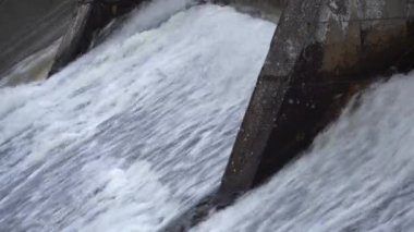 Beton şelale çağlayanı üzerinde dalgalanan güçlü su akışının yakın bir görüntüsü. Suyun yoğun hareketi ve güçlü gücü büyüleyici ve dinamik bir görsel etki yaratır..