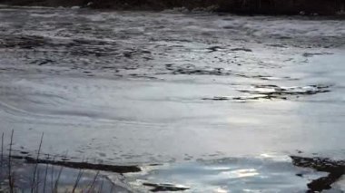 Hızla akan bir nehir batan akşam ışığını yakalar ve dalgalanan yüzeyinde dinamik yansımalar yaratır. Çalkantılı su akışı daha sakin köpükle kaplı yamalarla çelişiyor.