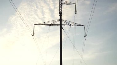 Yüksek voltajlı elektrik hattı kulesi bulutlu bir akşam gökyüzünün arka planına karşı dimdik ayakta duruyor. Bir yapının karmaşık tasarımı ve birleşen elektrik hatları çarpıcı bir teknolojik karşıtlık yaratır..