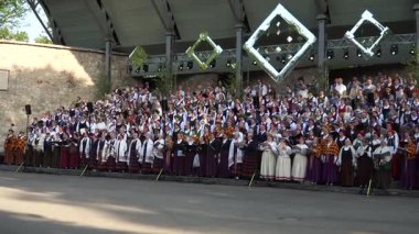 Dobele, Letonya - 27 Mayıs 2023. Geleneksel halk kostümlü büyük bir Letonya karışık korosu, ulusal çaptaki Letonya Şarkı Festivali sırasında açık havada şarkı söyleyerek koro mirasını kutluyor..