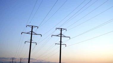 Sabahın erken saatlerinde kırsal kesimde tarlalar boyunca uzanan yüksek voltajlı elektrik hattı altyapısı görülüyor. Yüksek sütunlar açık sabah gökyüzüne karşı çarpıcı çizgiler oluşturur..