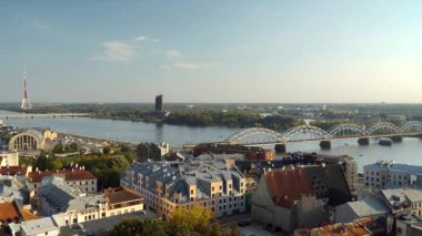 Riga 'nın şehir manzarası, Daugava Nehri, kemerli bir demiryolu köprüsü ve uzak mesafedeki yüksek televizyon kulesi ile birlikte, Latvias' ın tarihi ve modern mimarinin karışımını sergiliyor. Hava görünümü.