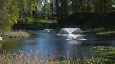 Şelalelerle süslenmiş huzurlu bir nehir şehir ortamında esiyor. Yaz güneşinin parlak ışığı, akan su, mimari tasarım ve doğal çevre arasındaki etkileşimi vurgular.