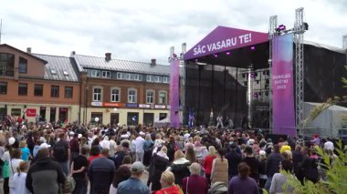 Dobele, Letonya - 3 Haziran 2023. Enerjik bir açık hava konserinin keyfini çıkaran kalabalık bir kasaba meydanı. Müzisyenler sahnede gösteri yaparak yaz festivali için canlı bir ortam yaratıyorlar..