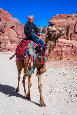 04 March 2020, Wadi Musa, Jordan: Bedouin man riding a camel adorned with colourful blankets at the ancient site of Petra in Jordan. Meedle East travel destination clipart