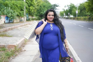 Genç Hintli, elinde alışveriş torbalarıyla sokakta yürüyen iri yarı bir kadın. Şişman kadın alışveriş yapıyor..