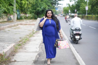 Genç Hintli, elinde alışveriş torbalarıyla sokakta yürüyen iri yarı bir kadın. Şişman kadın alışveriş yapıyor..