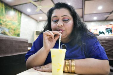 Genç ve cüsseli Hintli bir kadın restoranda oturmuş smoothie içiyor..