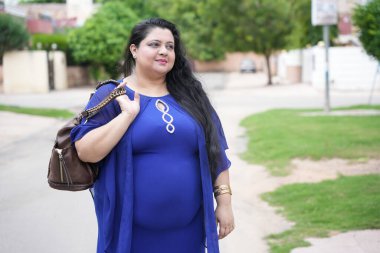 Mutlu genç Hintli artı cüsseli kadın sokakta duran deri el çantası tutuyor..