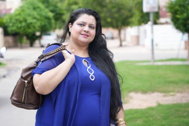 Mutlu genç Hintli artı cüsseli kadın sokakta duran deri el çantası tutuyor..