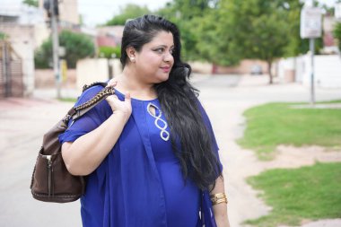 Genç Hintli artı cüsseli bir kadın sokakta duran deri el çantası tutuyor..