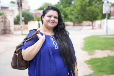 Mutlu genç Hintli artı cüsseli kadın sokakta duran deri el çantası tutuyor..