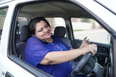 Emniyet kemeri takmadan araba kullanırken cep telefonuyla konuşan Hintli bir kadın..