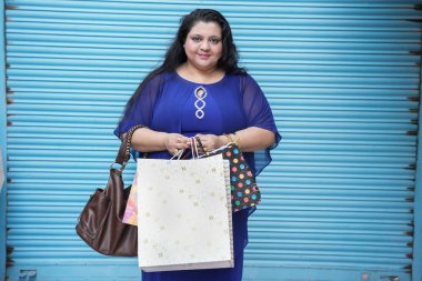 Mavi arka planda izole edilmiş alışveriş torbaları taşıyan genç Hintli kadın. Kilolu kadın alışverişi. konsept.