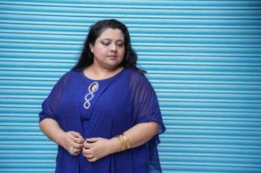 Mavi arka planda tek başına duran genç Hintli artı boyut kadın portresi..