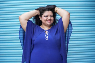 Mavi arka planda tek başına duran genç Hintli artı boyut kadın portresi..