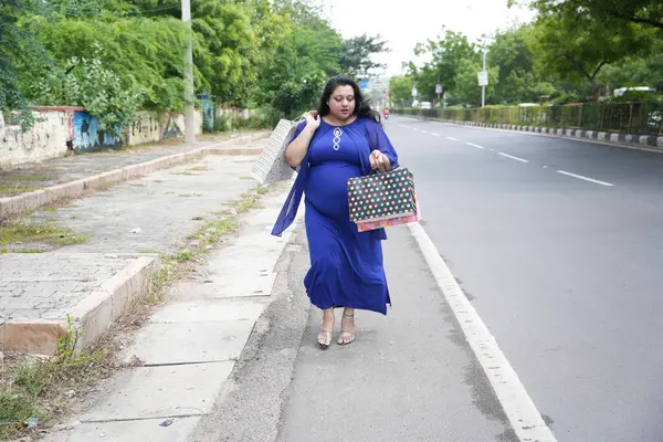 Genç Hintli, elinde alışveriş torbalarıyla sokakta yürüyen iri yarı bir kadın. Şişman kadın alışveriş yapıyor..