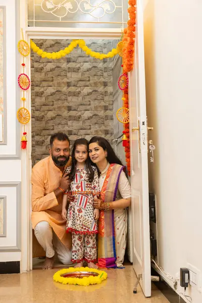 Happy indian family of three doing grah pravesh ritual or entering new house for the first time. Family sitting in front of a plate filled liquid kumkum and flowers. Griha Pravesh Concept
