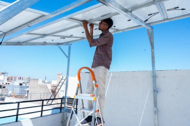 Hintli işçi evin çatısına güneş panelleri yerleştiriyor. Fotovoltaik panel sisteminin bakımı. Alternatif, yenilenebilir enerji kavramı.