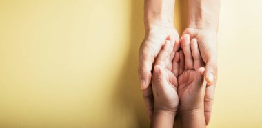 Üst düzey ebeveynler ve küçük çocuklar el ele tutuşuyorlar. Stüdyo çekimleri sarı arka planda, aile evinde izole edilmiş, çocukları yetişkin annelerin eline teslim ediyor, destek oluyor, aile günü kavramına destek oluyor.