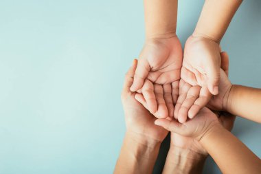 Üst düzey ebeveynler ve küçük çocuklar el ele tutuşuyorlar. Stüdyo çekimleri mavi arka planda, aile evinde izole edilmiş, çocukları yetişkin annelerin eline teslim ediyor, destek oluyor, aile günü kavramına destek oluyor.