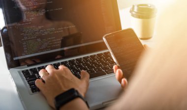 Software developer hands typing data coding programming javascript with laptop computer and mobile phone, Programmer woman looking smartphone program code at workplace, IT startup concept