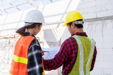 Mimar ve müvekkil, inşaat alanındaki binanın planıyla planı tartışıyor. Asyalı mühendis ustabaşı işçi ve kadın projeyi kontrol etmek için kağıt çizerek çalışıyorlar.