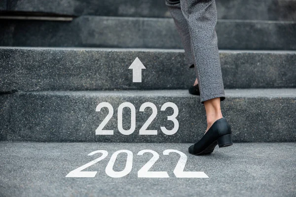Happy new year 2023. Stepping going up stairs in city, Closeup legs of businesswoman hurry up walking on stairway from 2022 to 2023, foot of business woman wear black shoes step up success next years