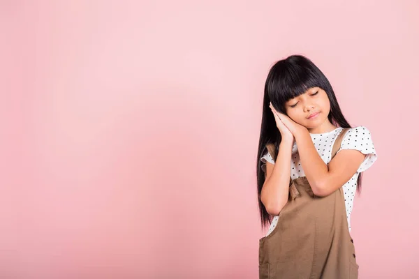 Asian little kid 10 years old standing with hands sealed pretending he is sleeping closed eyes at studio shot isolated on pink background, Happy child girl holding hands under face tired dreaming