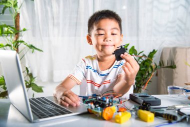 Küçük öğrenci elinde araba oyuncağı monte etmek için adım atan motor, Asyalı çocuk evde Arduino robot araba ev ödevi yapıyor, eğitim yapay zeka atölyesi dersi