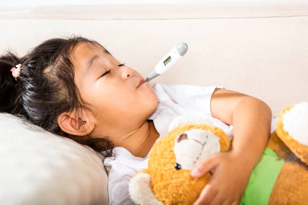 stock image Sick kid. Mother checking temperature of her sick daughter with thermometer in mouth, child laying in bed taking measuring her temperature for fever and illness