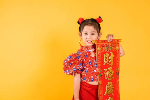 Chinese New Year. Happy Asian Chinese little child girl smile wearing red cheongsam qipao Spring festival couplets Character means fortune, blessing, studio shot isolated on yellow background