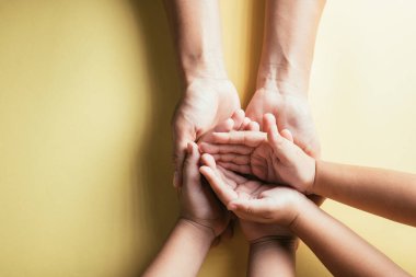 Üst düzey ebeveynler ve küçük çocuklar el ele tutuşuyorlar. Stüdyo çekimleri sarı arka planda, aile evinde izole edilmiş, çocukları yetişkin annelerin eline teslim ediyor, destek oluyor, aile günü kavramına destek oluyor.
