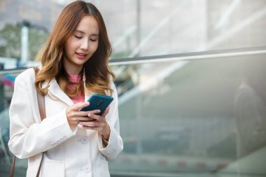 Asyalı iş kadını cep telefonunda yazı yazıyor ofisin yanındaki sokakta duruyor başarılı bir iş kadını portresi akıllı telefonu elinde tutarak sabah internet üzerinden sohbet ederek gülümsüyor.