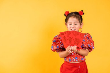 Çin Yeni Yılı. Mutlu Asyalı küçük kız gülümsemesi kırmızı cheongsam qipao tutun angpao kırmızı paket parasal hediye geleneksel elbise içinde portre çocuk, kısa sarı arka plan izole stüdyo