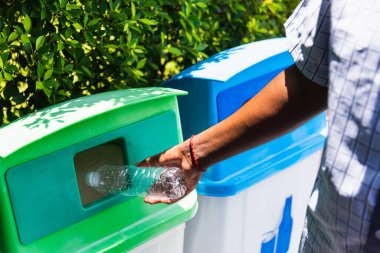 Seçici odak noktası siyah adamın boş plastik su şişesini çöp veya çöp kutusuna, çevresel geri dönüşüm konseptine atması.