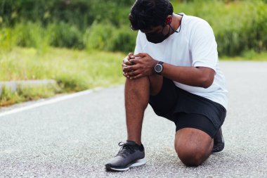 Kapatın Asyalı genç spor koşucusu. Siyah adam, el ele oturuyor. Açık hava sokak sağlık parkında koşarken diz ağrısı çekiyor.