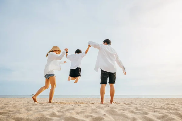 幸せなアジアの家族は ビーチで一緒に楽しく健康的なライフスタイルを生きています 家族の母親 父と息子が手を取り合って夜明け時に空中でジャンプする 家族の屋外活動のコンセプト — ストック写真