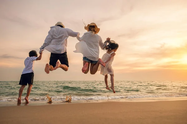 幸せな家族は 日没の休日にビーチで楽しいジャンプをしています 旅行や休暇を楽しんでいる人々に戻る 家族の父 娘のシルエット手をつないでビーチで一緒にジャンプする — ストック写真