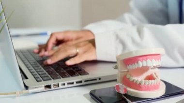 Üniformalı dişçi doktor ya da hemşire sözlü yazılım dişleri Xray ve bilgi tıbbi geçmiş formlarını kayıt için dizüstü bilgisayara, masada diş modeli, dişçilik konsepti için kullanıyor.