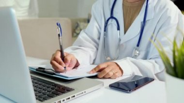Steteskoplu doktor ya da hemşire hasta hakkında bir şeyler yazıyor. Evrak listesindeki hasta bilgilerini panoya yazıyor ve hastaların bilgilerini dizüstü bilgisayara, reçeteli sağlık raporlarına yazıyor.