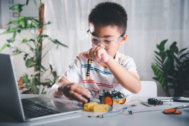 Küçük çocuk oyuncağı monte etmek için tornavidayla cevizi sıkıyor, Asyalı çocuk evde Arduino robot araba ev ödevi yapıyor, eğitim yapay zeka atölyesi dersi öğreniyor.